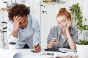 Casal preocupado analisa papéis, calculadora e celular em um ambiente de trabalho, expressando os efeitos emocionais da tomada de decisões financeiras no cotidiano, em uma situação que reflete os princípios das finanças comportamentais.