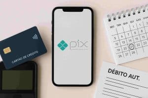 Imagem composta por elementos relacionados a finanças digitais no Brasil. Ao centro, um smartphone exibe a tela inicial do sistema de pagamentos instantâneos PIX, com a legenda “powered by Banco Central”. À esquerda, há um cartão de crédito e uma maquininha de pagamento, enquanto à direita estão um calendário com o dia 21 circulado e um formulário intitulado “DÉBITO AUT.”. A composição ilustra como o PIX mudou a forma de lidar com dinheiro no Brasil, promovendo praticidade nos pagamentos e na organização financeira.