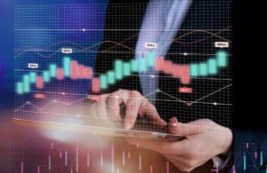 Pessoa utiliza um tablet enquanto gráficos de candlestick e linhas de tendência são projetados à frente, representando análises e operações típicas do mercado financeiro em ambiente digital e dinâmico.